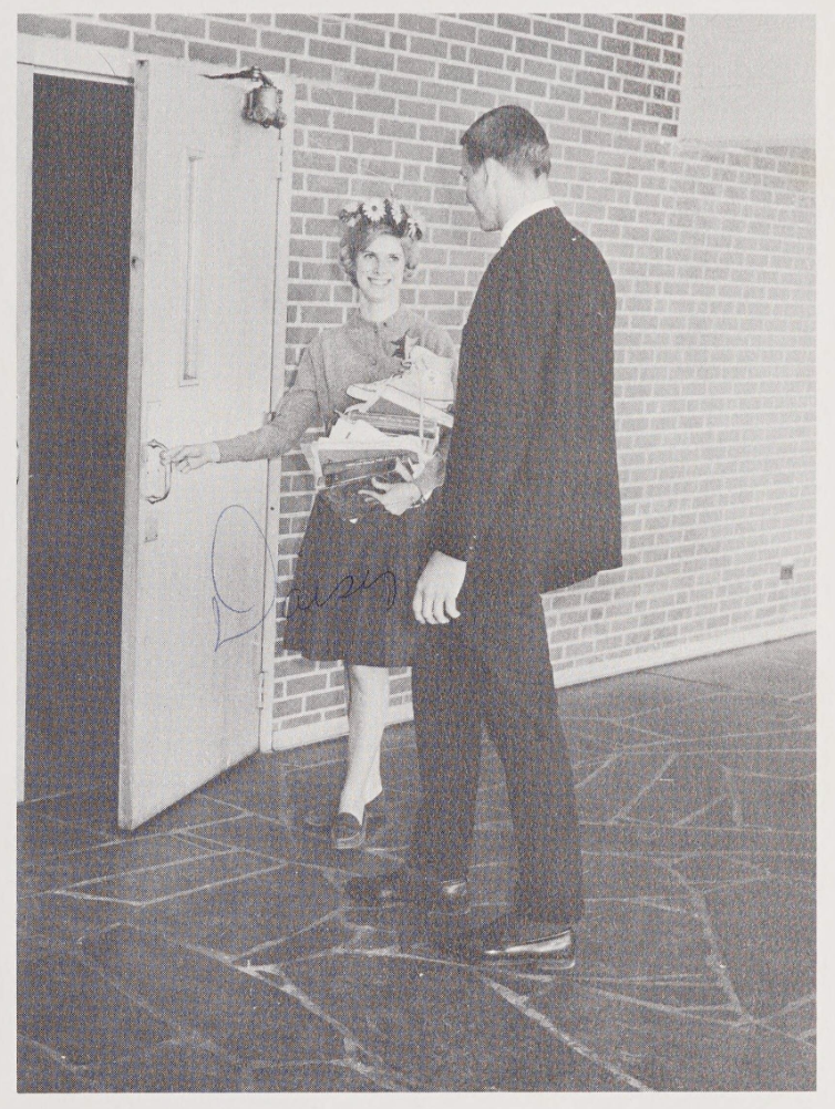 Betty Jo Swaim stands on the left, holding a door open. She was just crowned as "Daisy Mae" and has a flower crown on her head. She chose Wayne Lewis as her "Lil' Abner," and he stands to her right. 